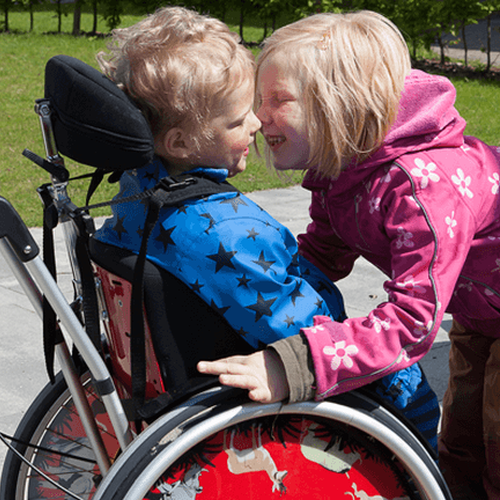 Zwei Kinder umarmen sich herzlich. Eins sitzt im Rollstuhl (Foto: Kleinert GfG).